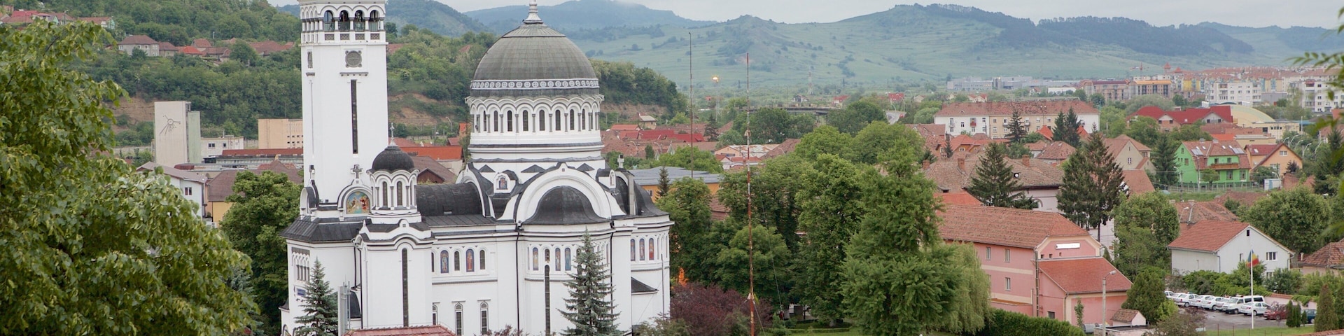A white church with a bell tower and dome, surrounded by trees and houses.