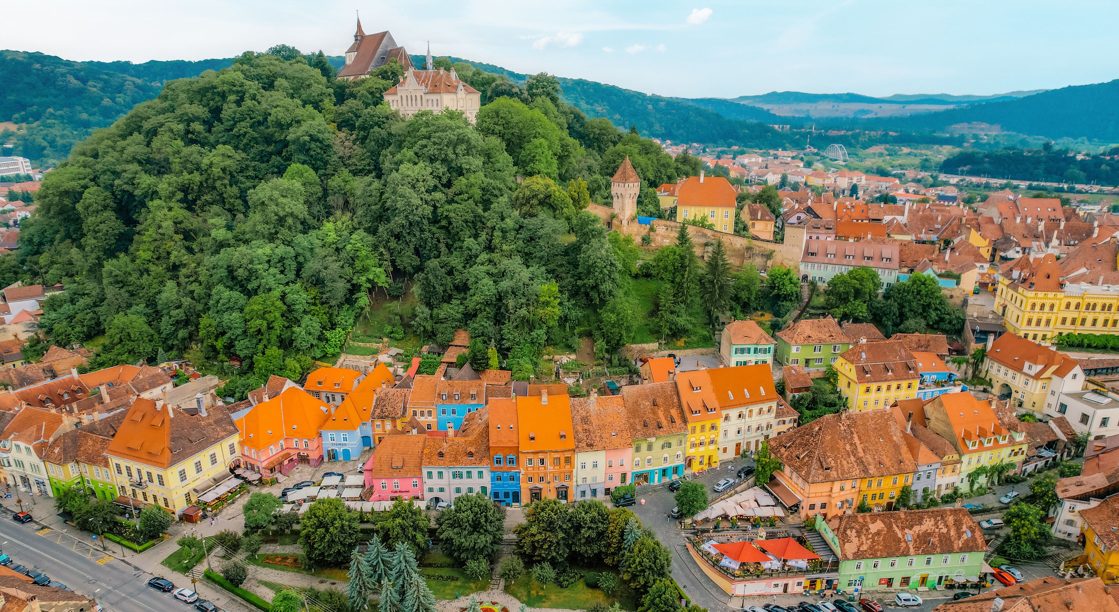A town with colorful buildings, a castle on a hill, and a river in the background.