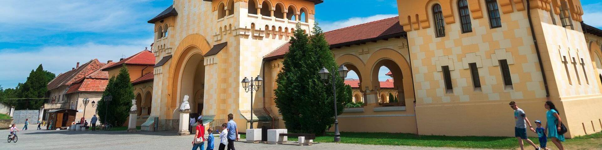 A historic building with a prominent tower, arched walkways, and a clear blue sky.