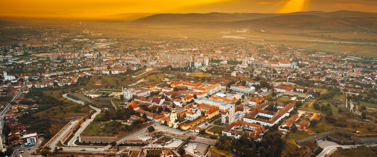 An aerial view of a town with a prominent castle, surrounded by residential areas and a hilly landscape.