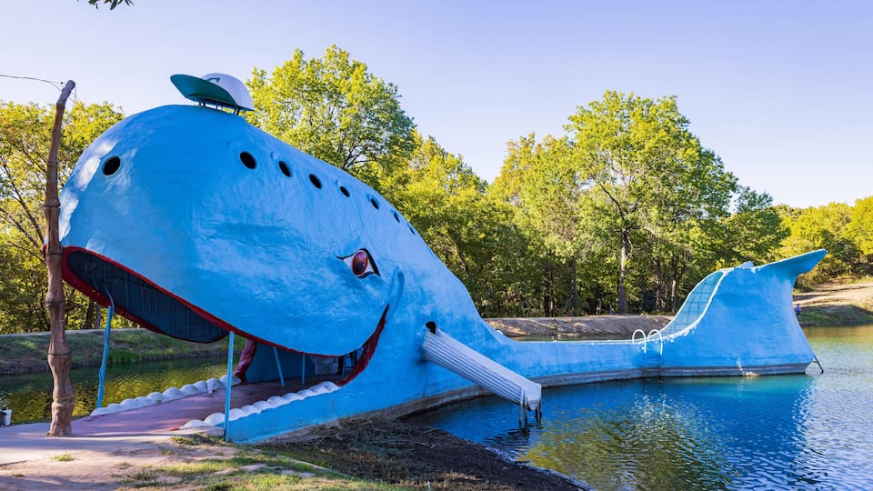 A large blue whale sculpture by a lake surrounded by trees.
