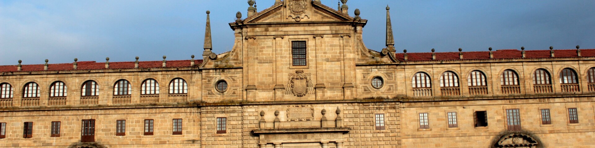 Un edificio histórico grande con una entrada central, múltiples ventanas y un tejado de tejas rojas.