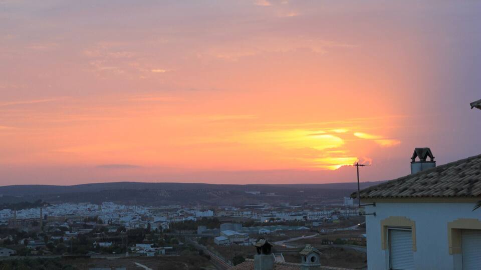 A sunset over a town with buildings and hills in the background.