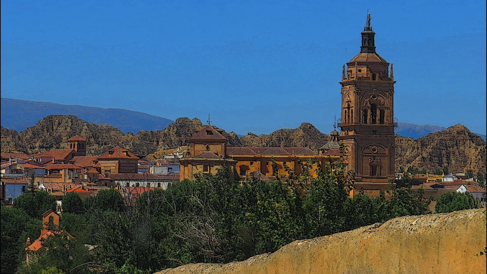 A historic town with a prominent clock tower, surrounded by rugged hills and a clear blue sky.