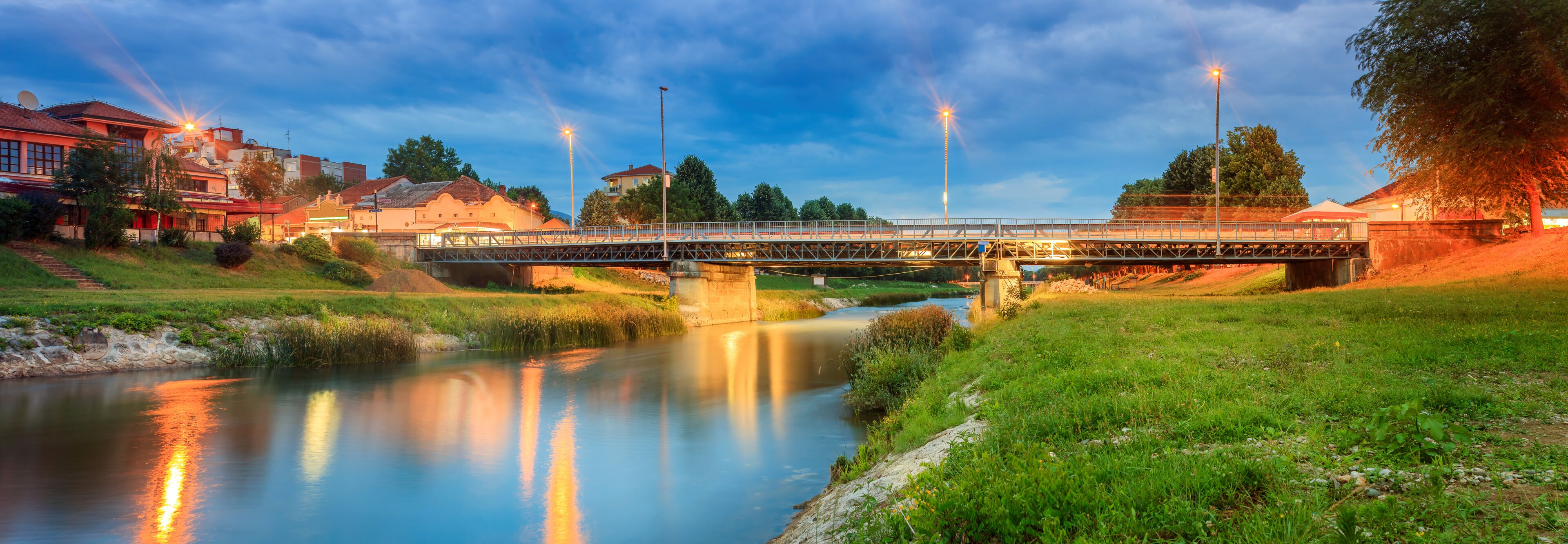 A bridge over a river with surrounding greenery and buildings.