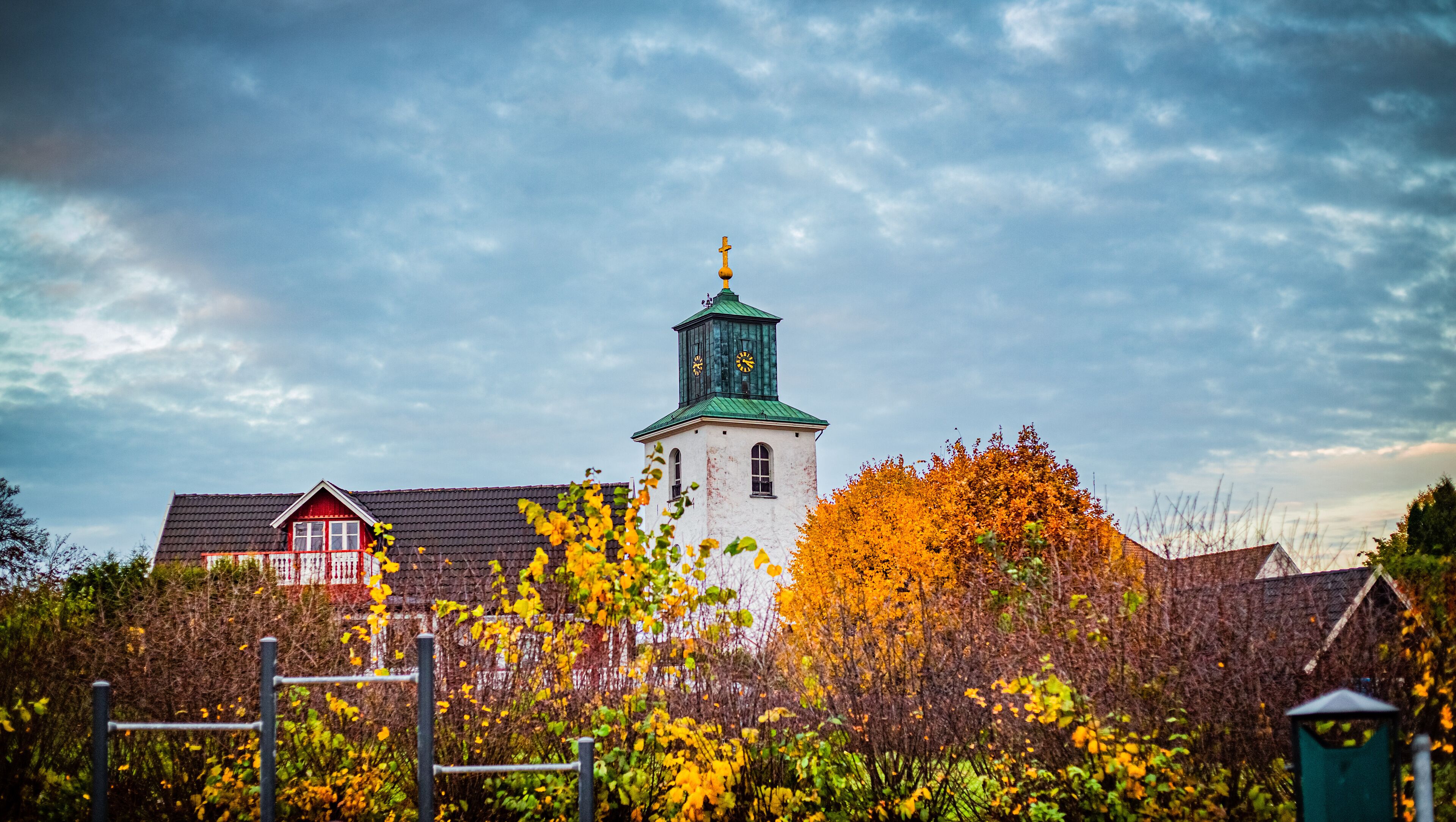 A church with a clock tower, surrounded by autumn foliage and residential buildings.
