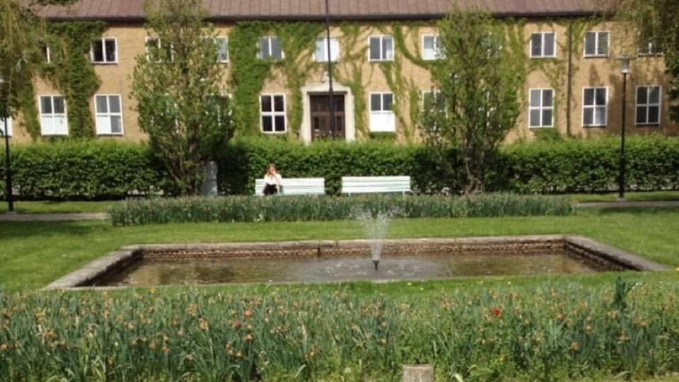 A building with a garden in front, a fountain, and a bench.