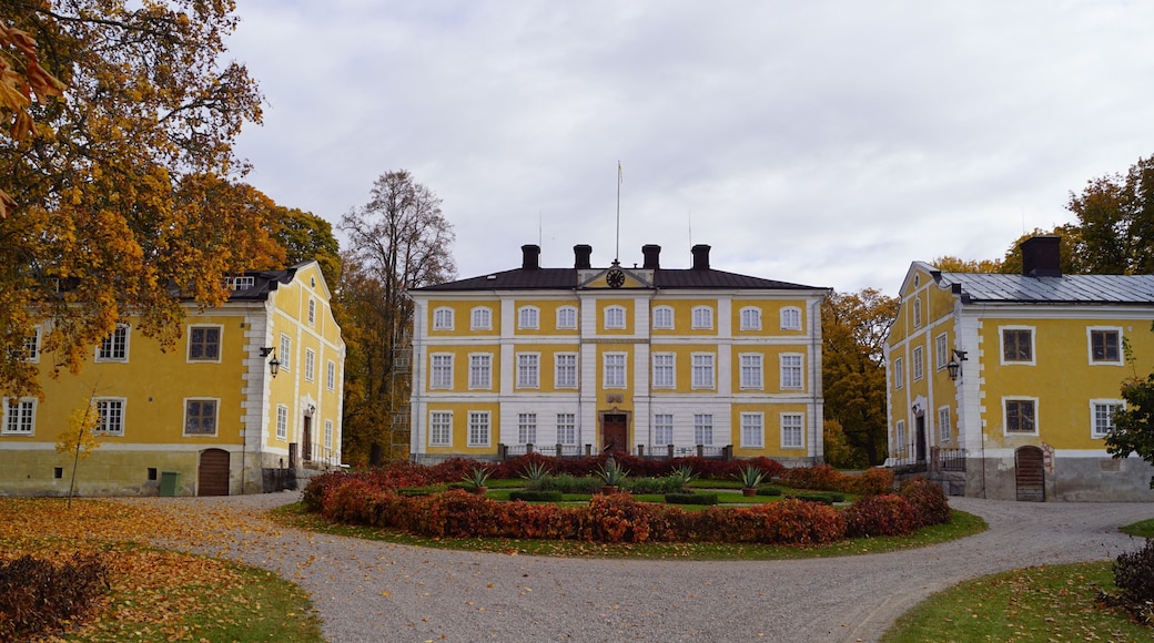 A large yellow building with a symmetrical facade, surrounded by a gravel path and a well-maintained garden with autumn foliage.