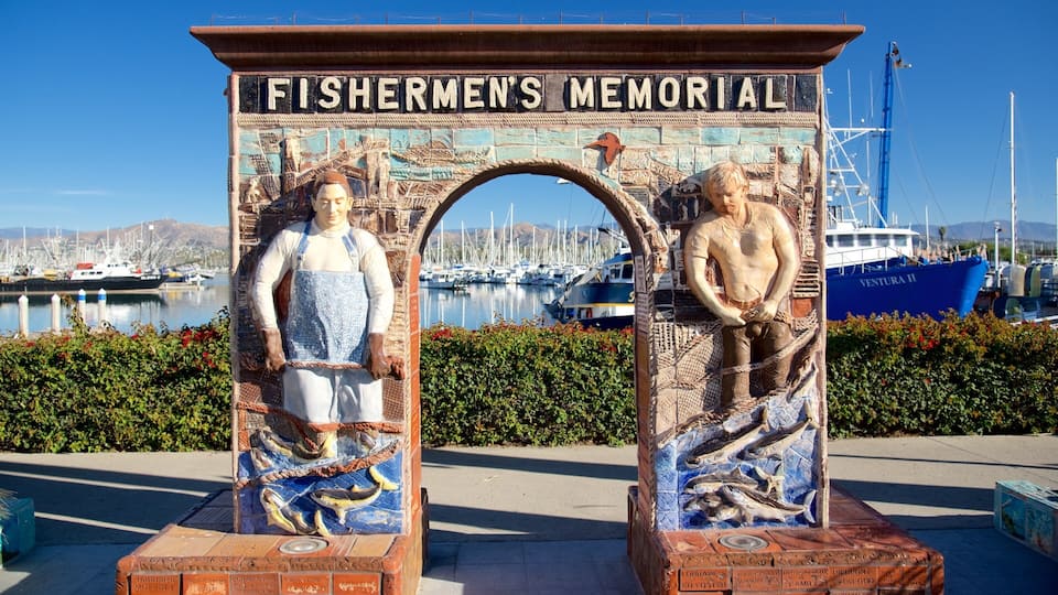 Fishermen's Memorial with two statues, a harbor, and boats in the background.