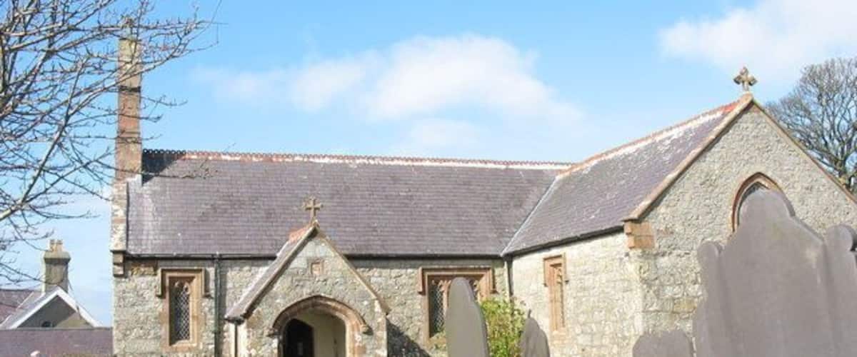 A stone church with a cross on the roof, an arched entrance, and several gravestones in the foreground.