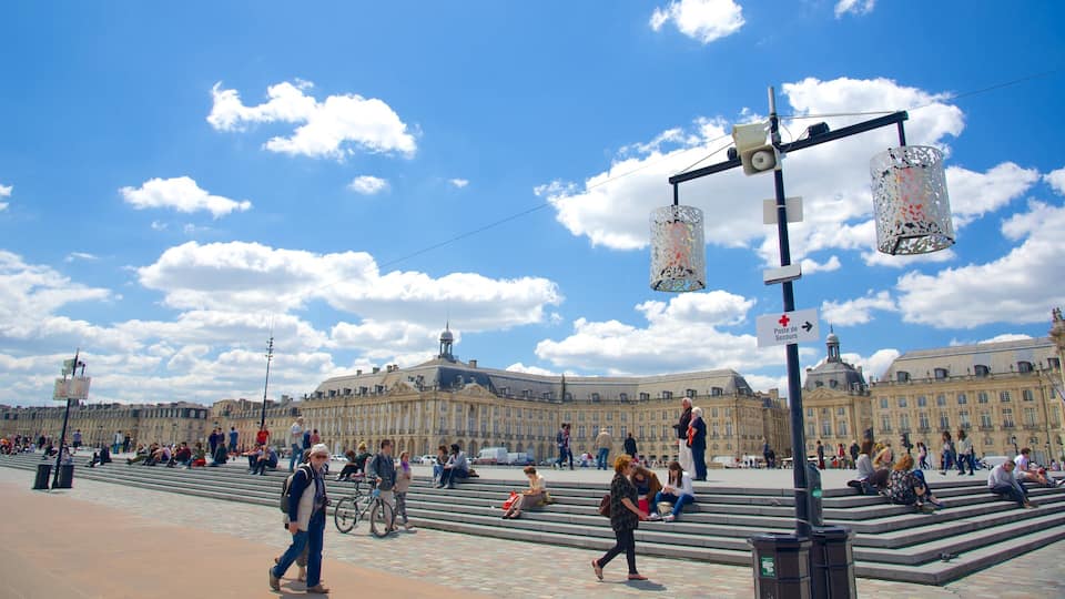 A busy public square with steps leading up to a large historic building, a clear blue sky, and a street sign indicating a postal service.