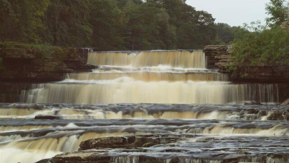 A multi-tiered waterfall surrounded by dense forest.
