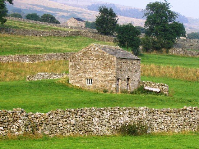 A stone house in a rural field with stone walls and green grass.