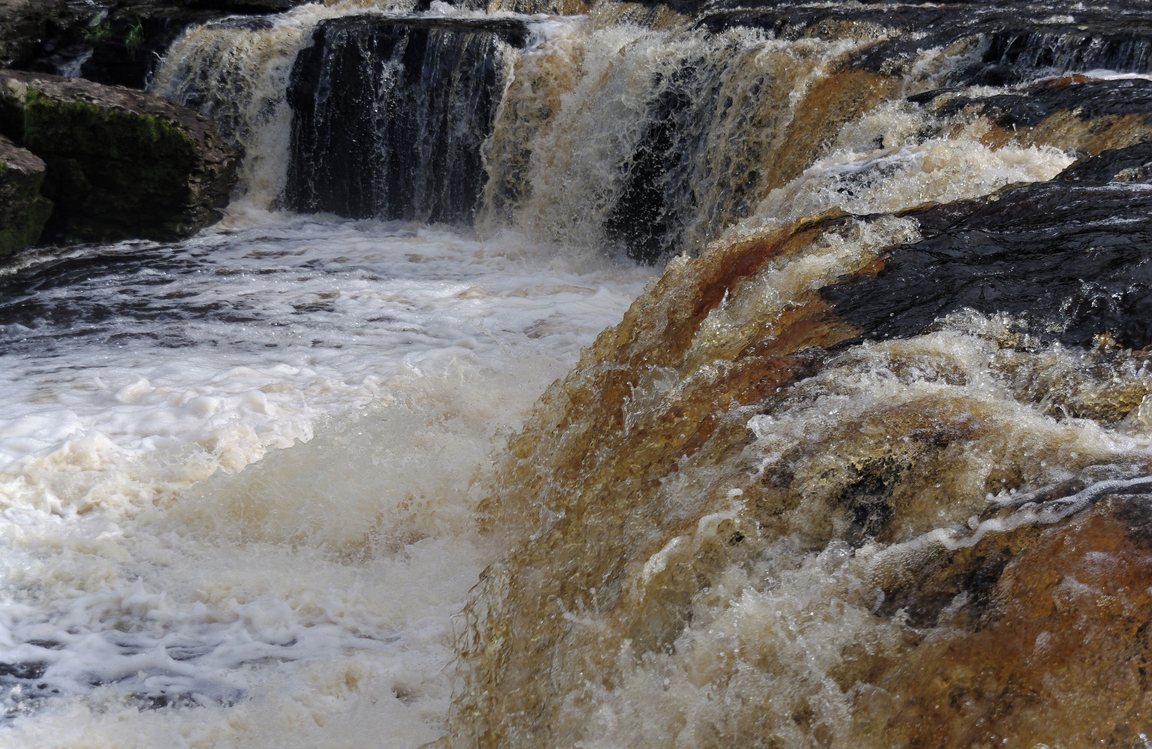 A turbulent waterfall with cascading water over dark rocks.