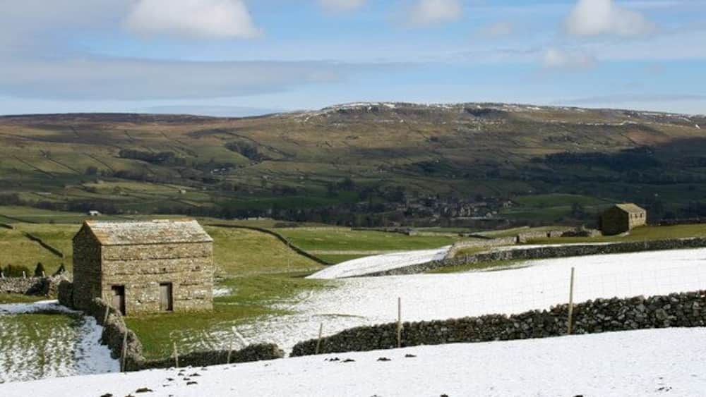 A snow-covered landscape with a stone building and rolling hills in the background.