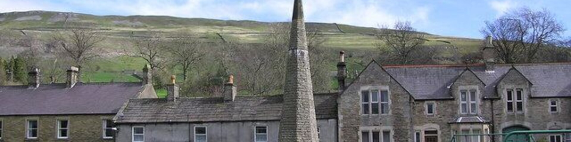 Un monumento de piedra en un área verde con casas al fondo.