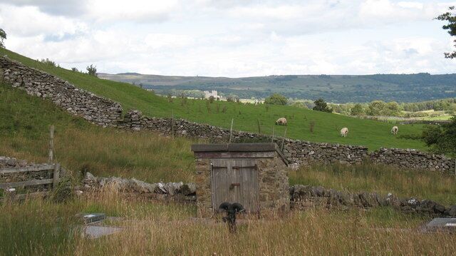 A stone wall, a wooden structure, and grazing sheep in a rural landscape.