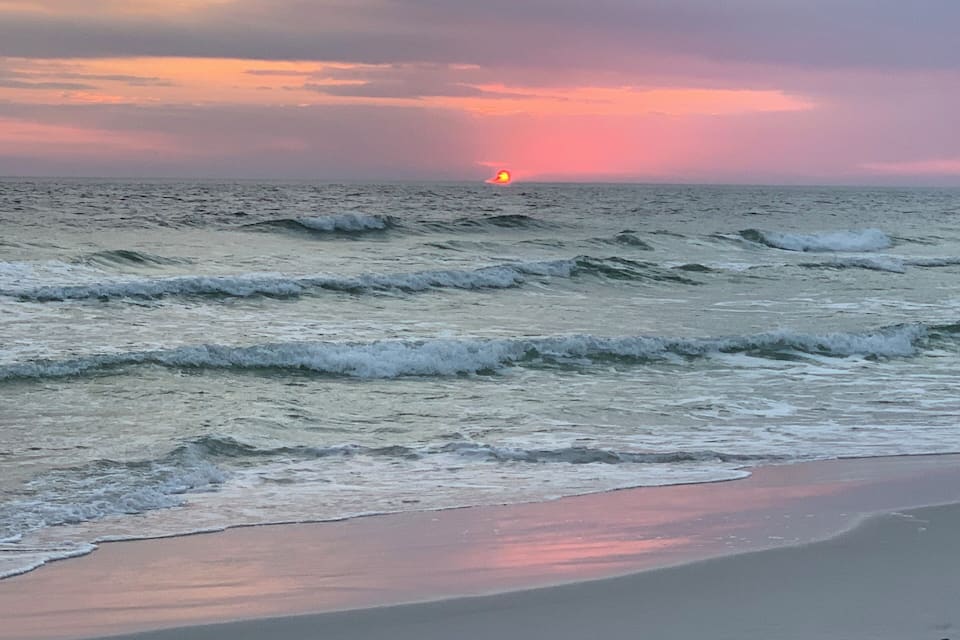 A beach with waves and a sunset in the distance.