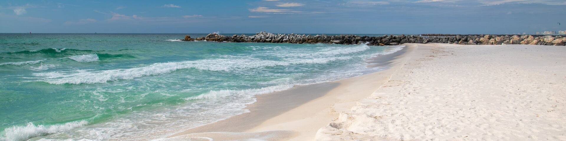 A beach with white sand, turquoise water, and a rocky breakwater.