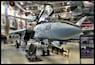 Un avion militaire portant le numéro 204 sur le nez, garé à l’intérieur d’un hangar avec d’autres avions, et un panneau d’exposition en arrière-plan.