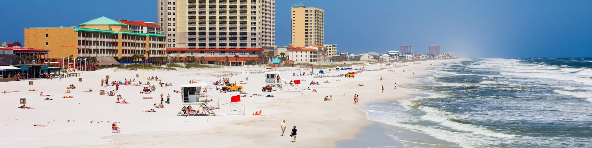 A beach with waves, people, and buildings in the background.