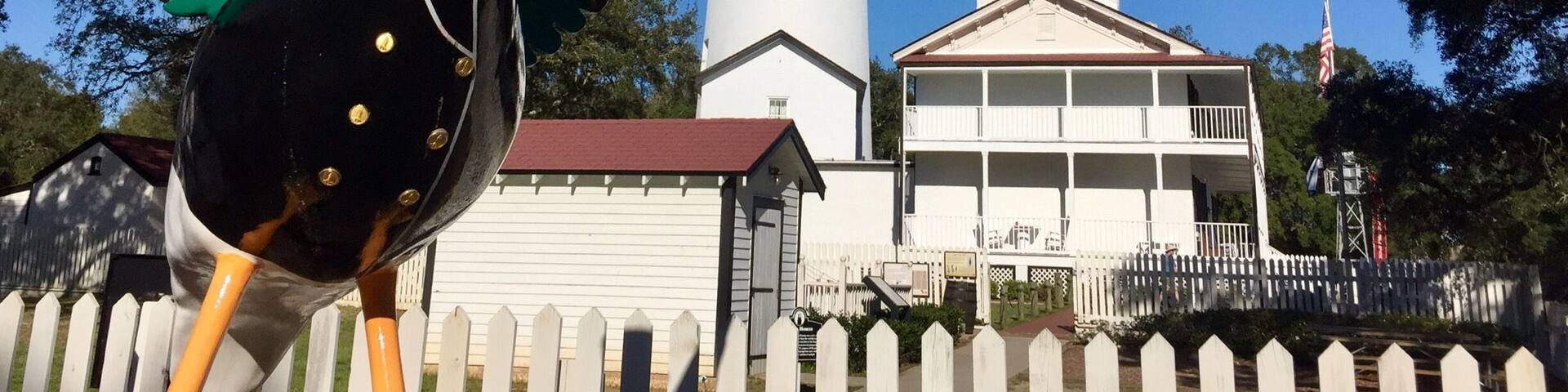 A lighthouse, a large bird sculpture, and a white house with a red roof.