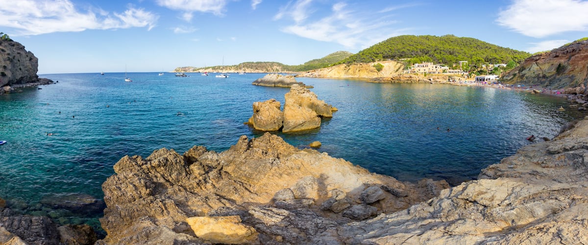 A coastal landscape with rocky outcrops, clear blue water, and boats.