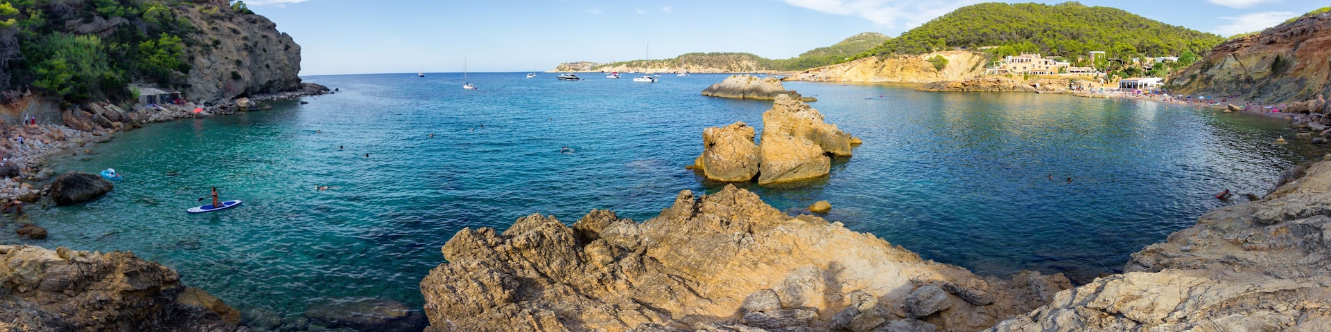A coastal landscape with rocky outcrops, clear blue water, and boats.