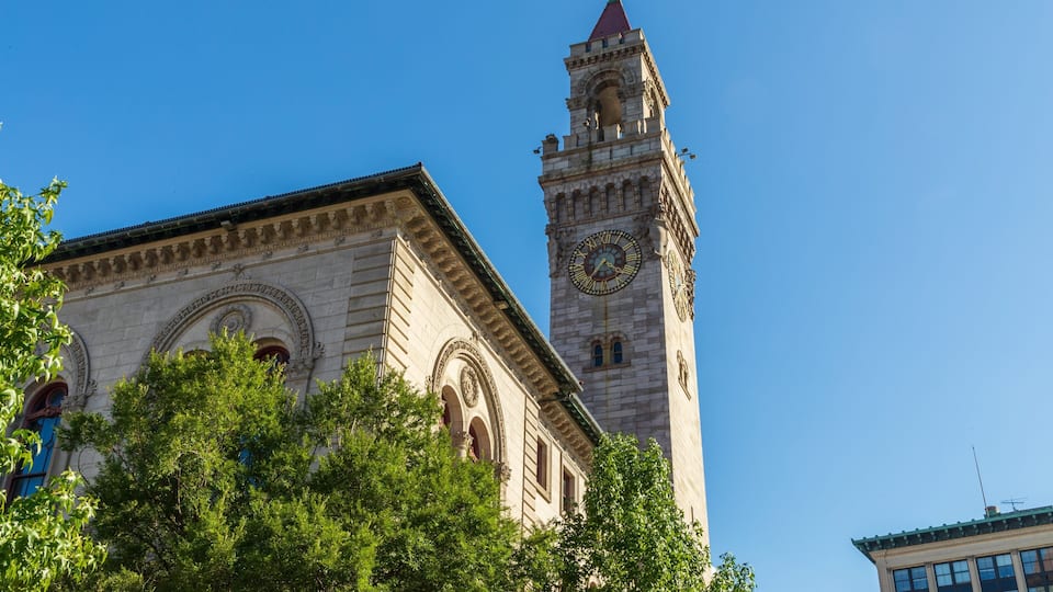 A historic building with a clock tower and lush green trees in the foreground.