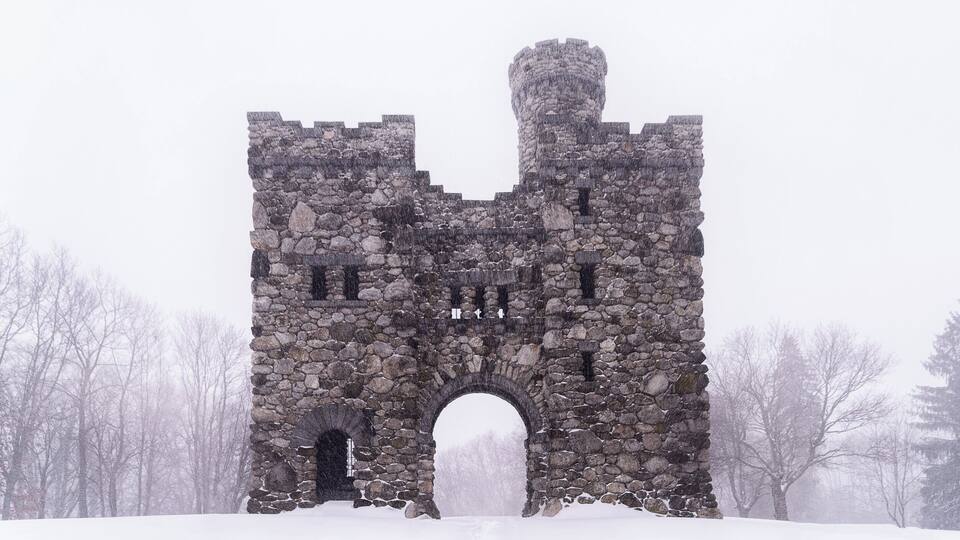 Eine steinerne Burg mit einem großen Bogen, umgeben von schneebedeckten Bäumen.