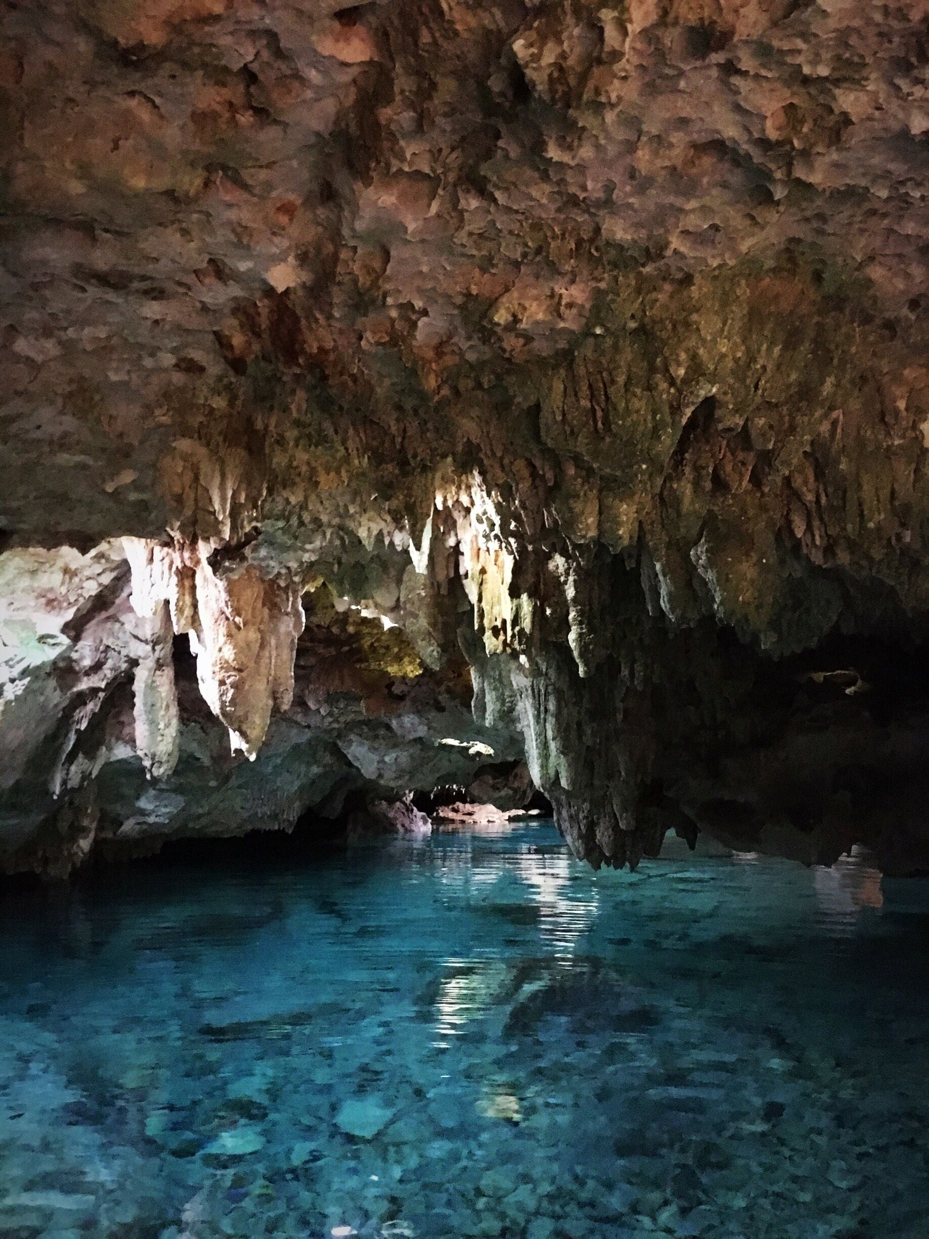 A cave with stalactites and stalagmites, clear water, and a rocky ceiling.