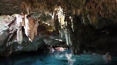 Una cueva con estalactitas y estalagmitas, agua cristalina y un techo rocoso.