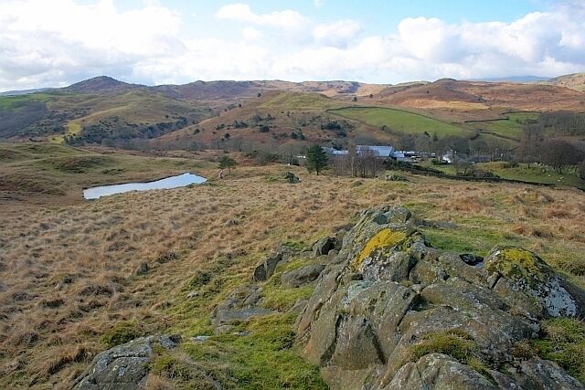 Un paisaje montañoso con un lago pequeño, afloramientos rocosos y un edificio lejano.