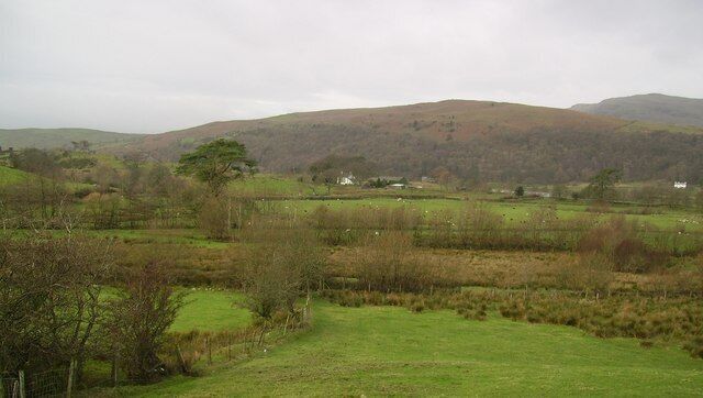A rural landscape with rolling hills, a fenced field, and scattered trees.