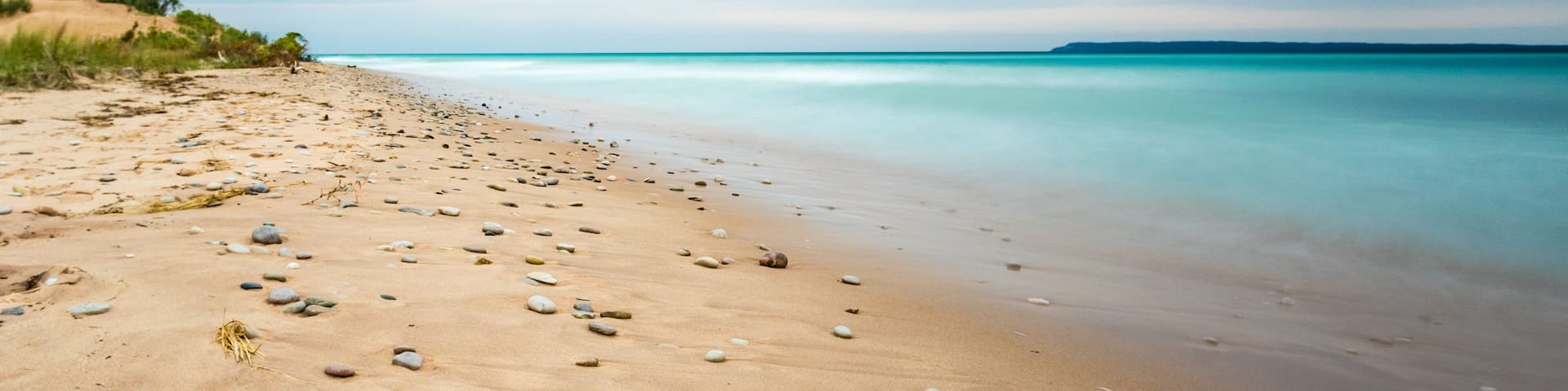 A sandy beach with scattered rocks and calm turquoise waters.