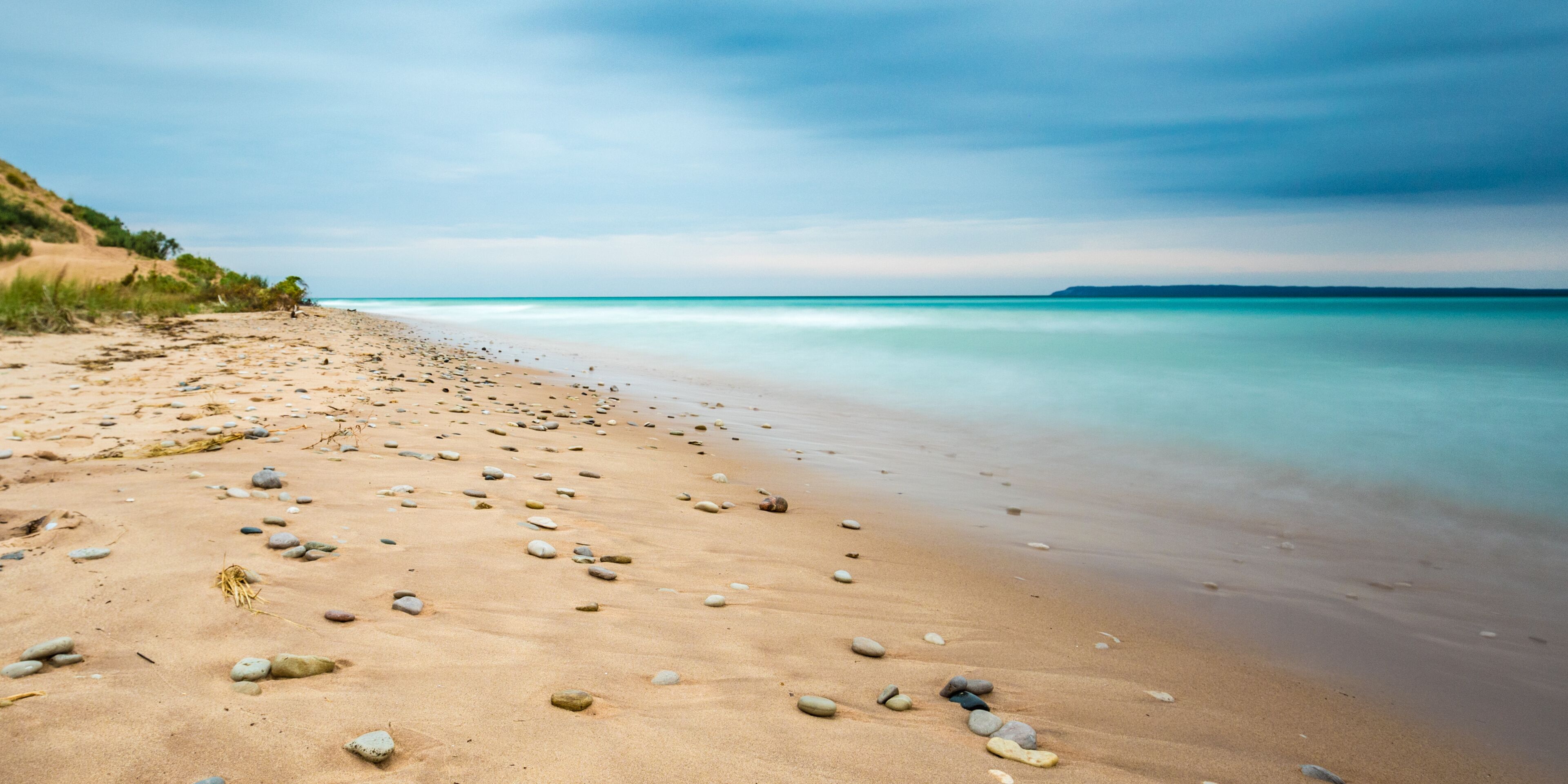 A sandy beach with scattered rocks and calm turquoise waters.