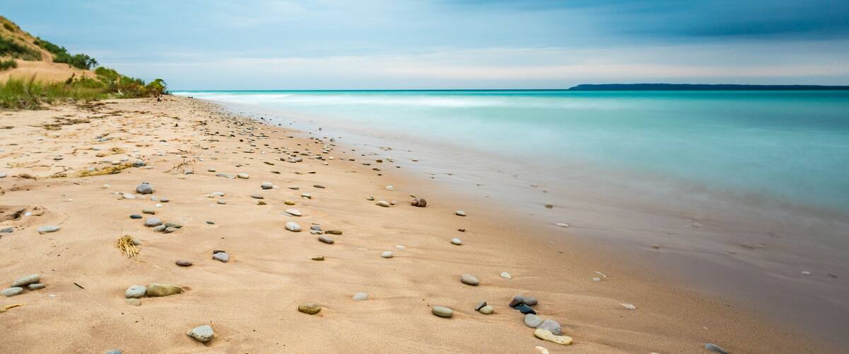 A sandy beach with scattered rocks and calm turquoise waters.