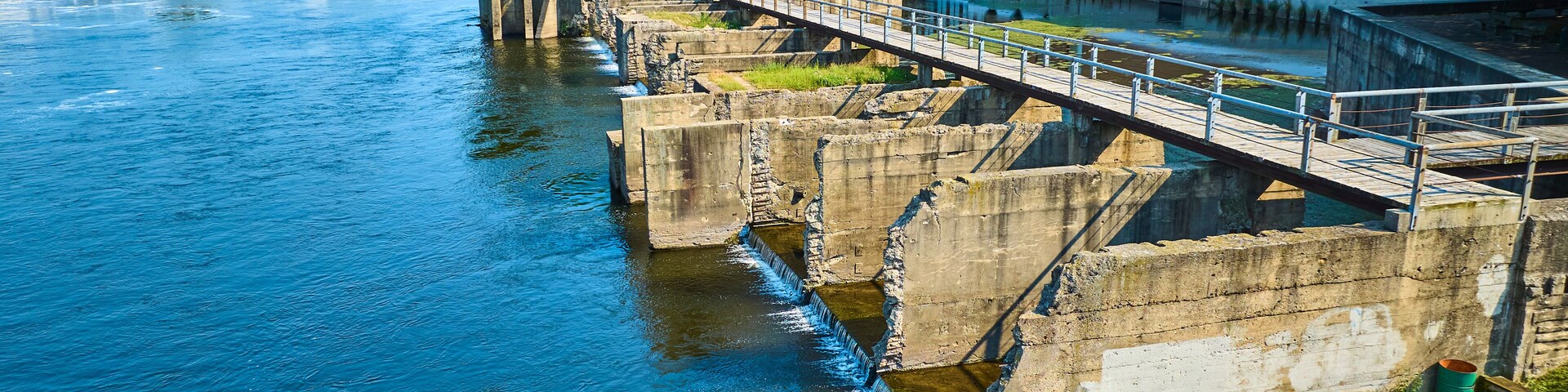 Um rio com um sistema de eclusas de concreto, uma ponte e um edifício moderno com grandes janelas.