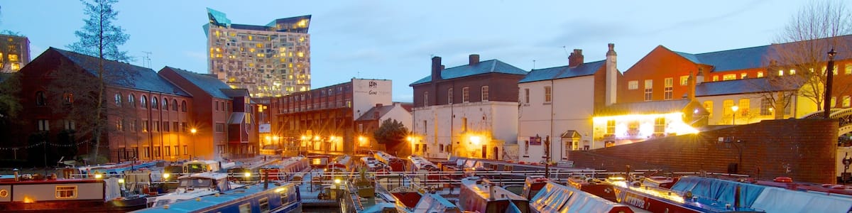 A marina with several narrowboats docked in calm water, surrounded by buildings and a modern high-rise in the background.