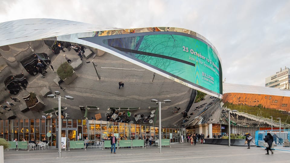 A modern building with a curved facade and a large digital billboard advertising an event.