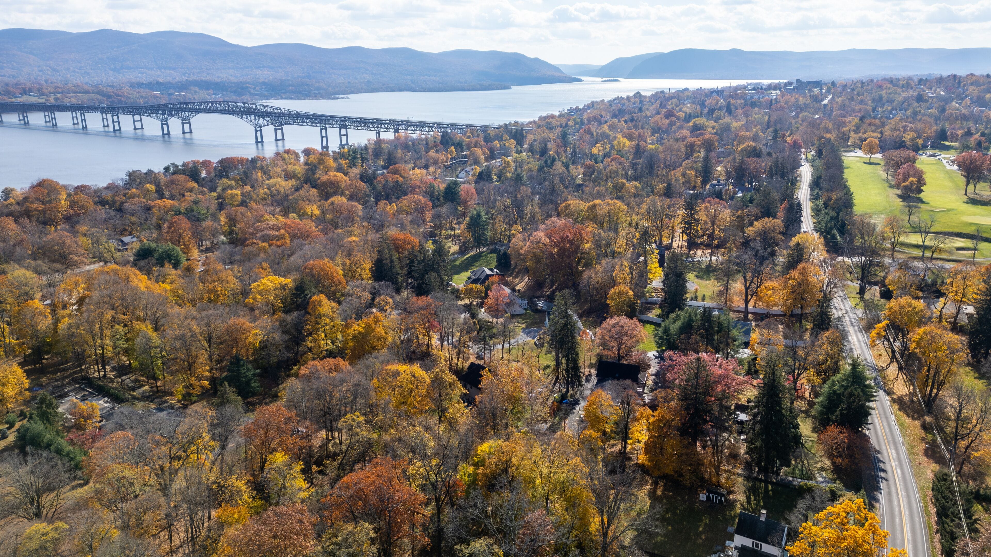 Golf course near Newburgh NY with panoramic fall colors, rolling fairways, and river in background. Captures scenic beauty, symmetry, and tranquility of a suburban recreational landscape.