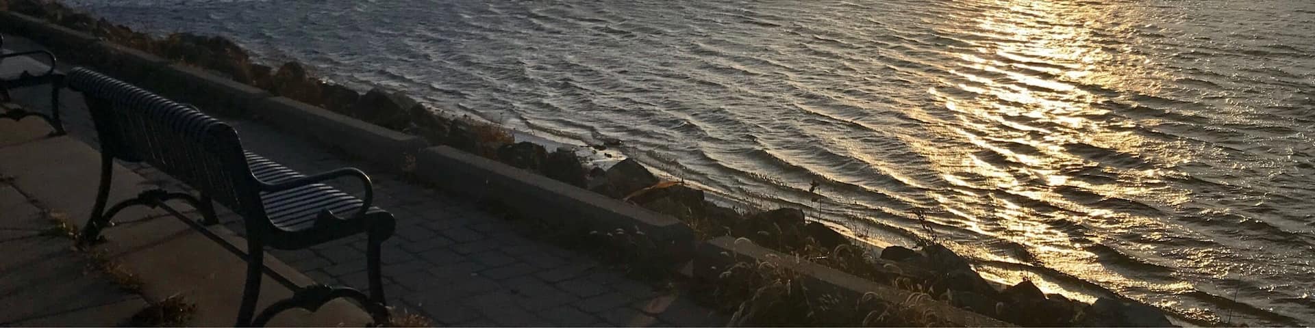 Un atardecer sobre un río con un puente y un banco a lo largo de la orilla.