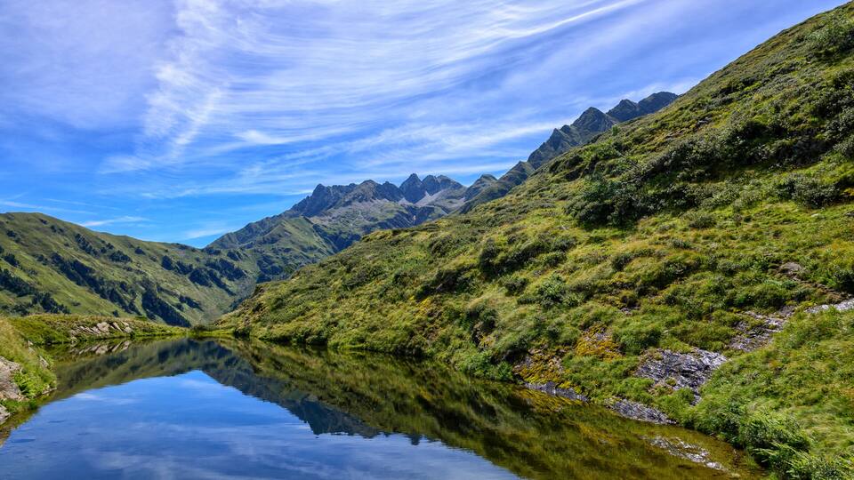 A mountain landscape with a clear lake reflecting the sky and surrounding hills.