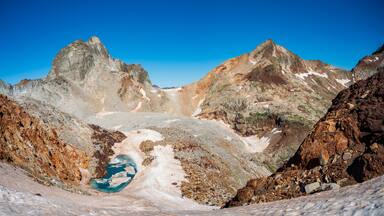 Peaks Gourgs Blancs and Gourdon in symmetry over small blue frozen lake and snow tongue. Pyrenees. France.