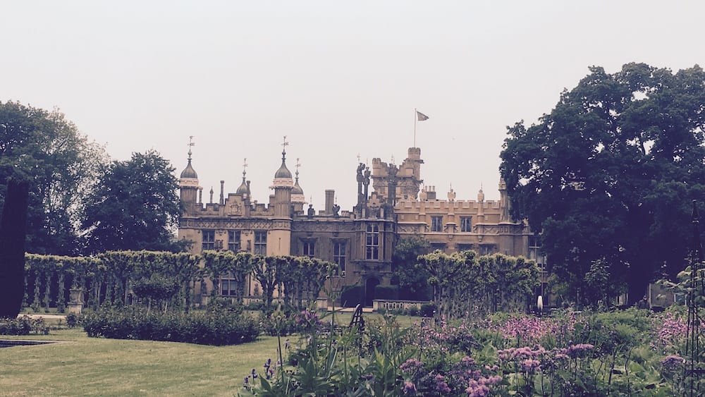 A grand castle with turrets and a flag, surrounded by lush gardens and trees.
