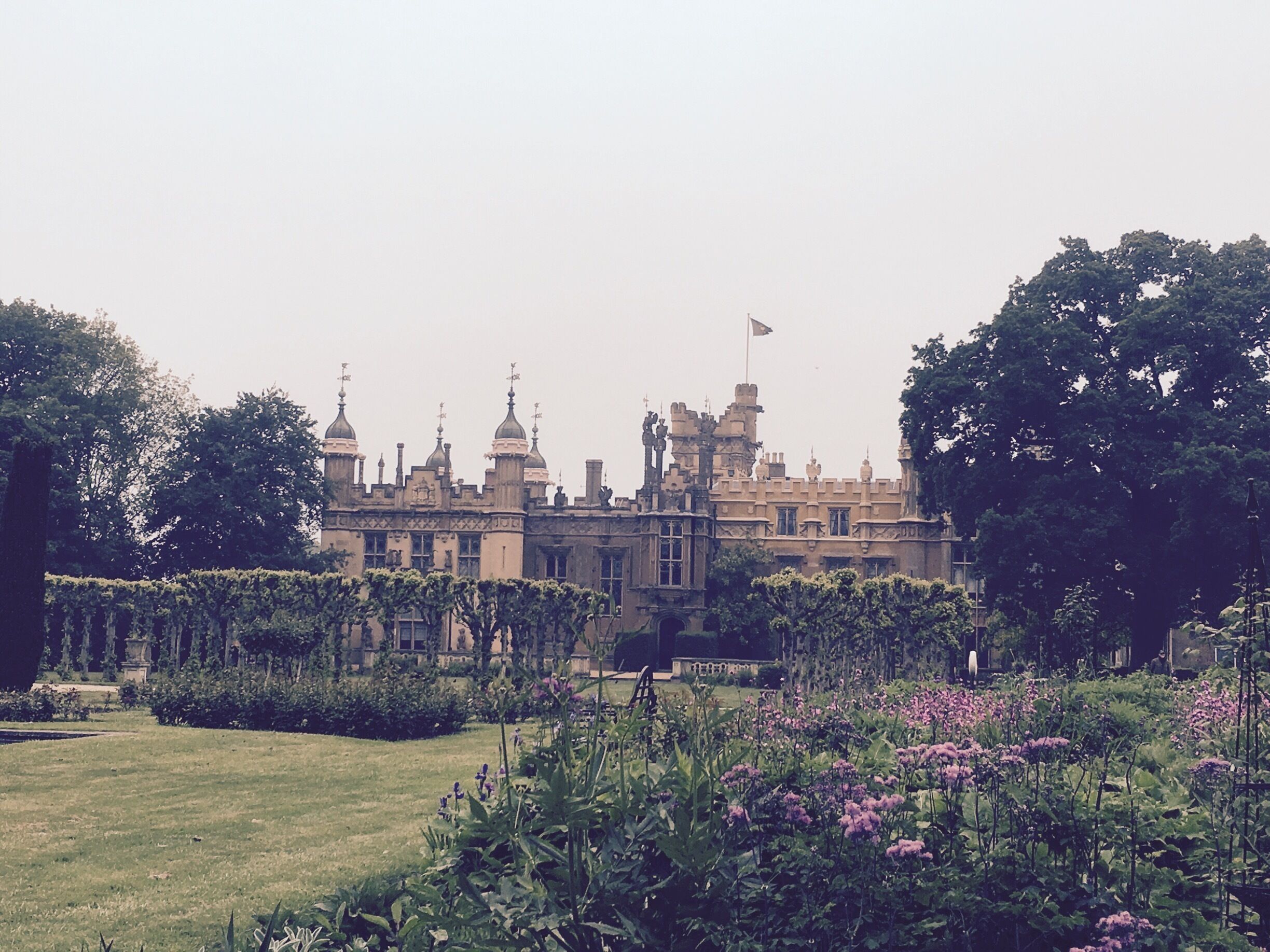 A grand castle with turrets and a flag, surrounded by lush gardens and trees.