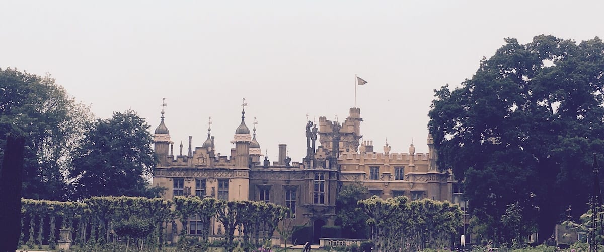A grand castle with turrets and a flag, surrounded by lush gardens and trees.
