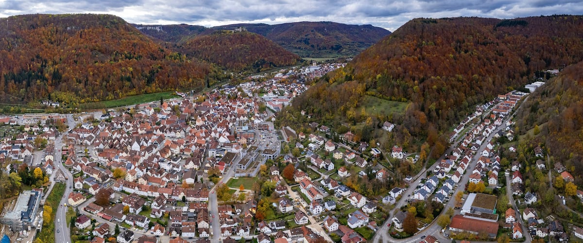 A town nestled in a valley with autumn-colored trees and mountains in the background.