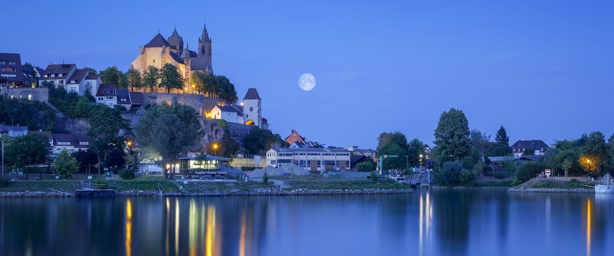 A moonlit lake with a historic castle and modern buildings in the background.