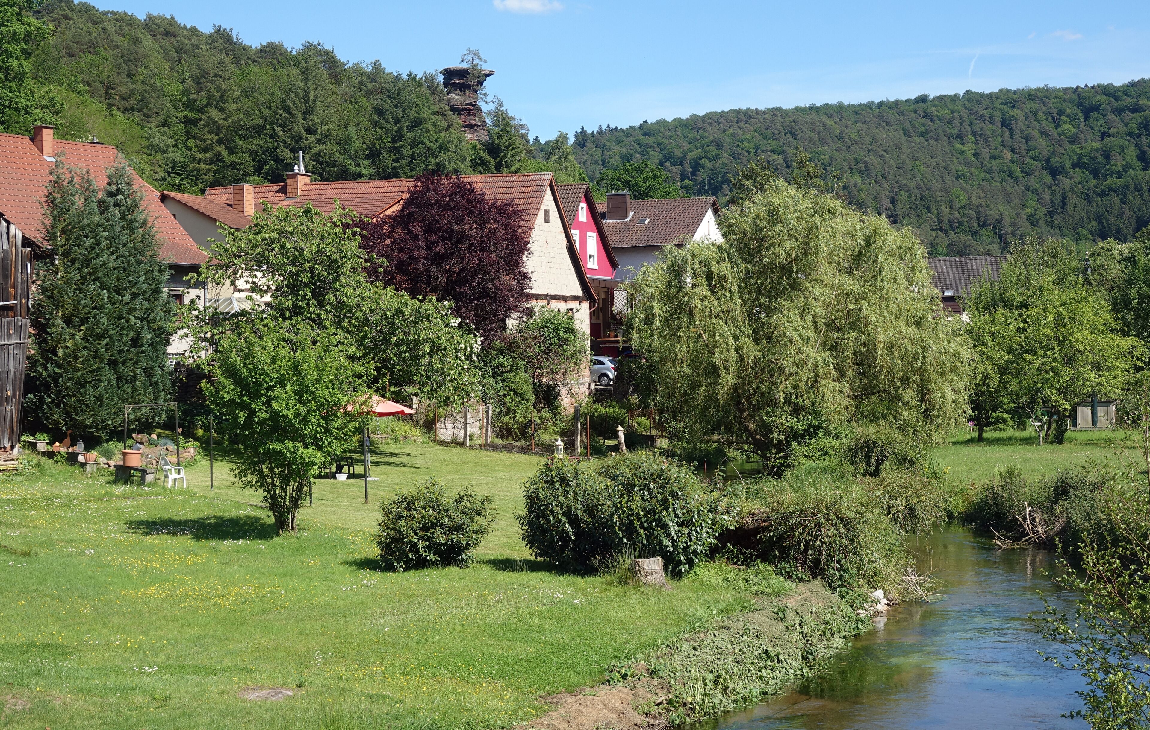 A village with houses, a river, and a forested hill in the background.